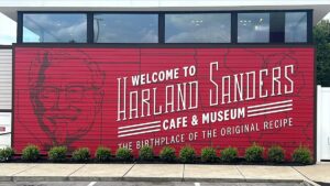A wall mural that says "welcome to Harland Sanders Cafe and Museum the birthplace of the original recipe"