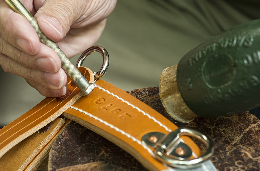 Close up photo of someone hand stamping part of a leather harness with numbers, using a metal tool