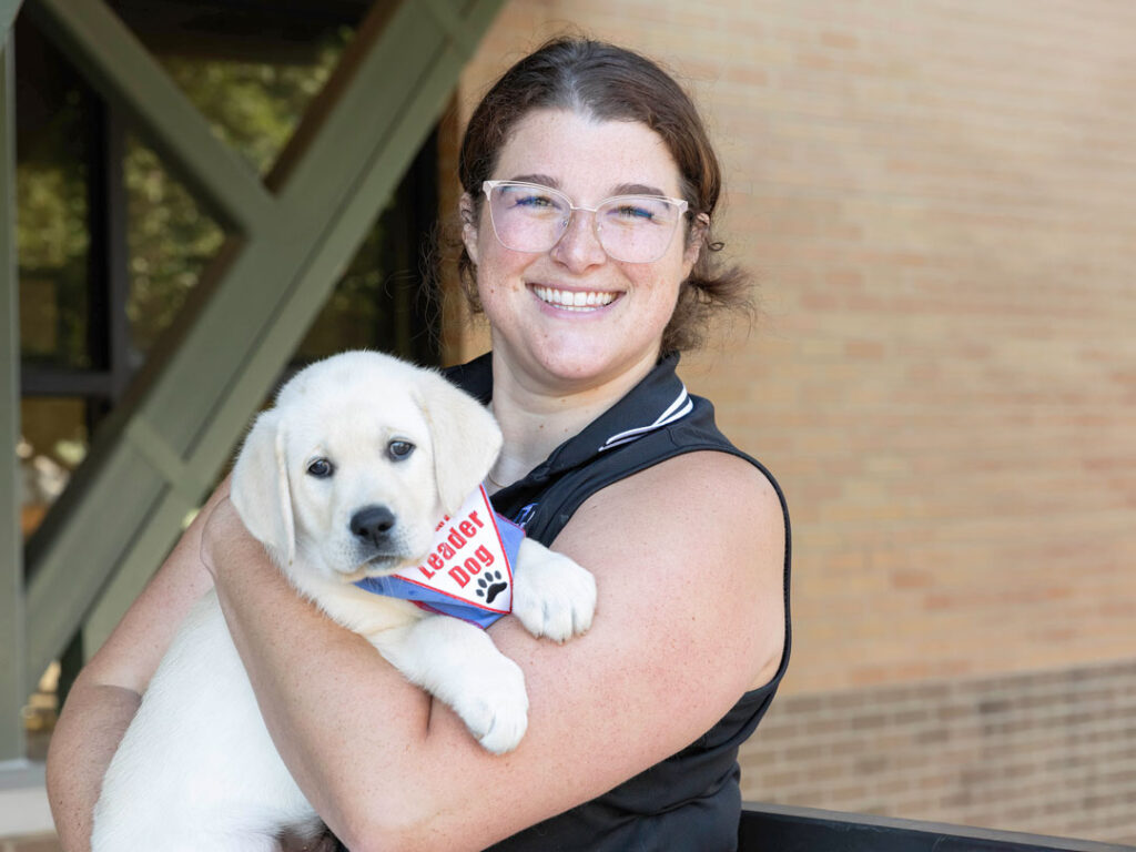 A person smiles while holding a fluffy puppy adorned with a 