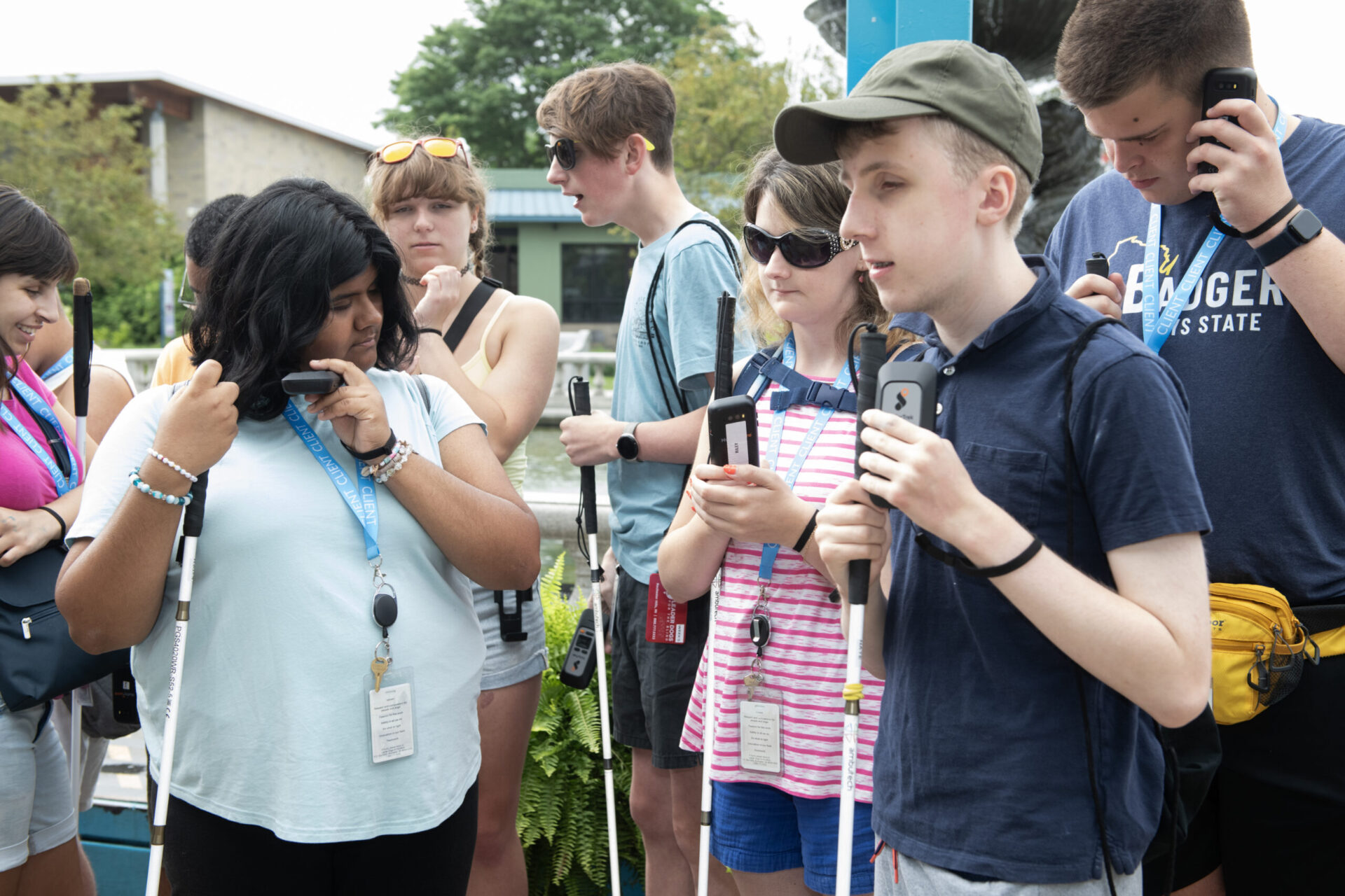 A group of young individuals gathers outdoors, each engaged with mobile devices while exploring their surroundings.