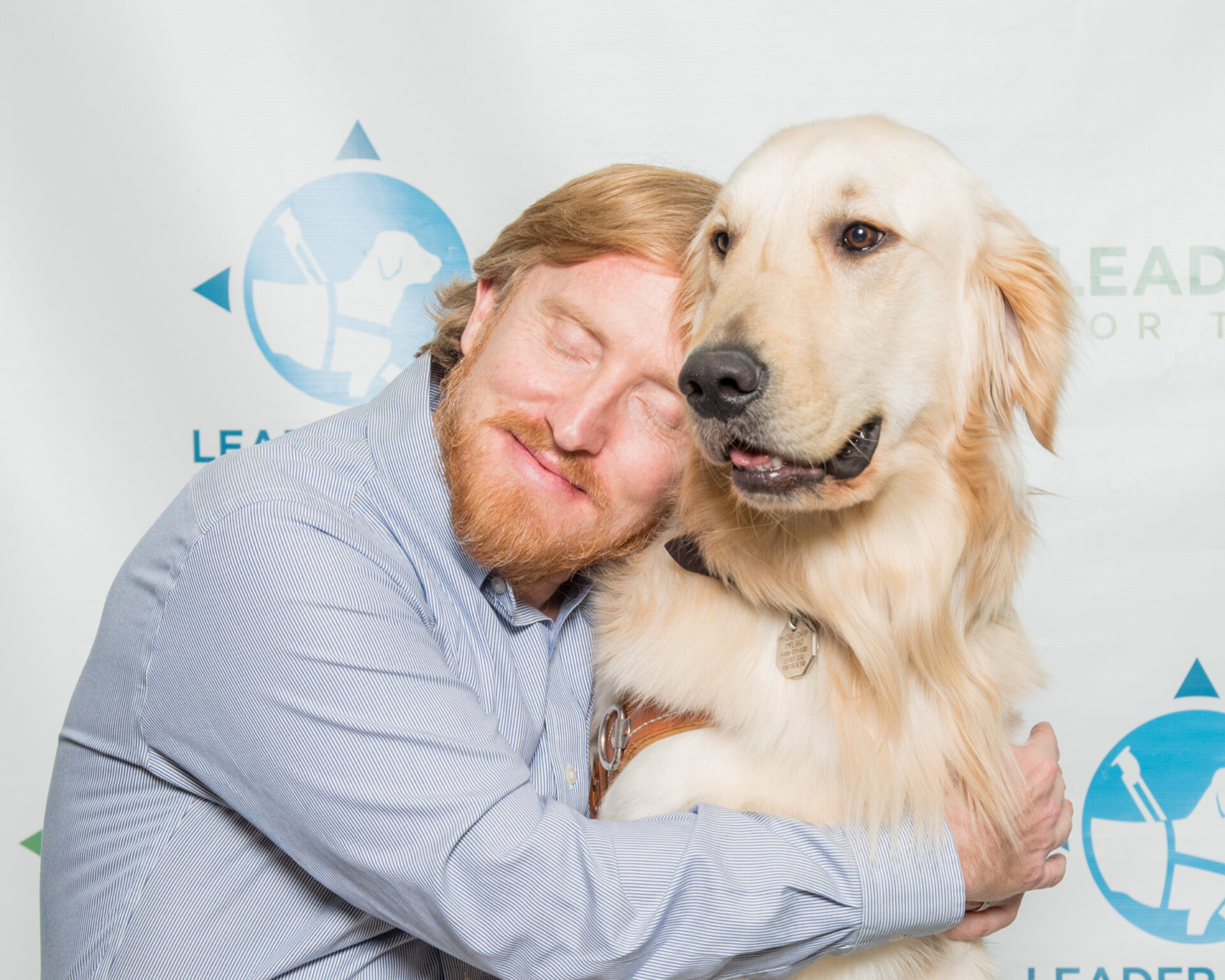 A man hugs a golden retriever guide dog, smiling warmly with his eyes closed.