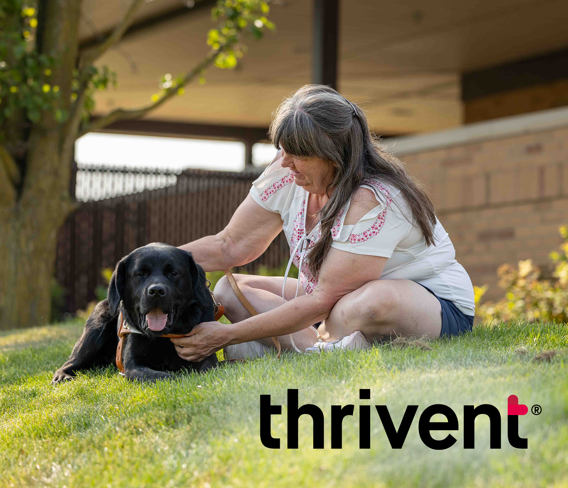 A person is sitting on a lawn, gently interacting with a large, friendly black dog. Thrivent logo in the bottom right corner.